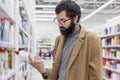 Young man in the supermarket in the household chemicals department. Large selection of products. A brunette with glasses and a bea Royalty Free Stock Photo